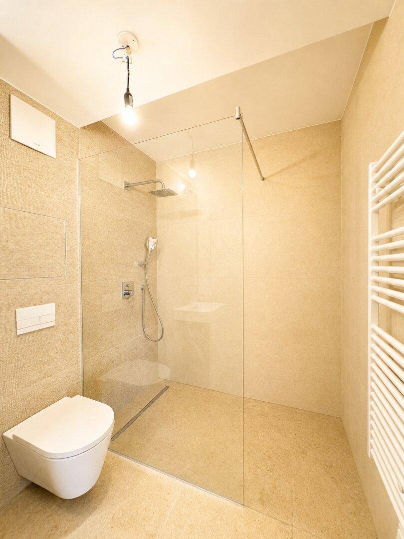 Modernes Badezimmer mit beigefarbenen Fliesen, ebenerdiger Dusche und wandhängender Toilette.