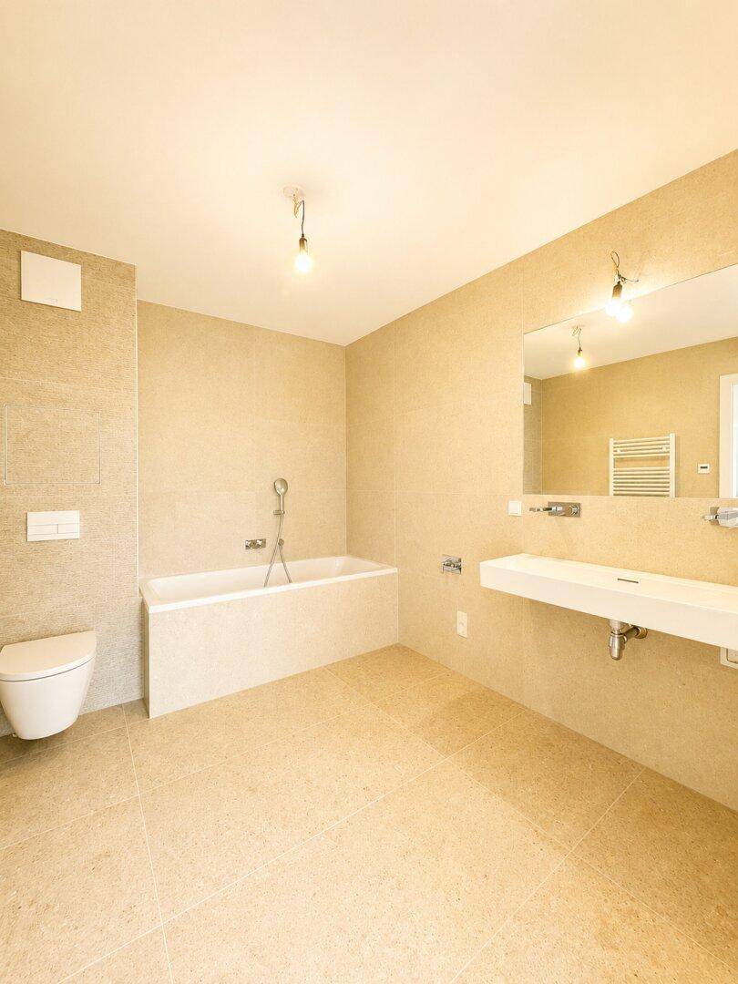 Modernes Badezimmer mit beigefarbenen Fliesen, Badewanne, Toilette und großem Waschbecken.