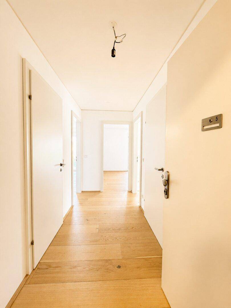 Heller Flur mit Holzboden und mehreren Türen, der zu weiteren Räumen führt.