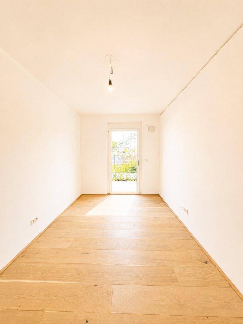 Leeres, helles Zimmer mit Holzboden und einer Tür, die ins Freie führt.