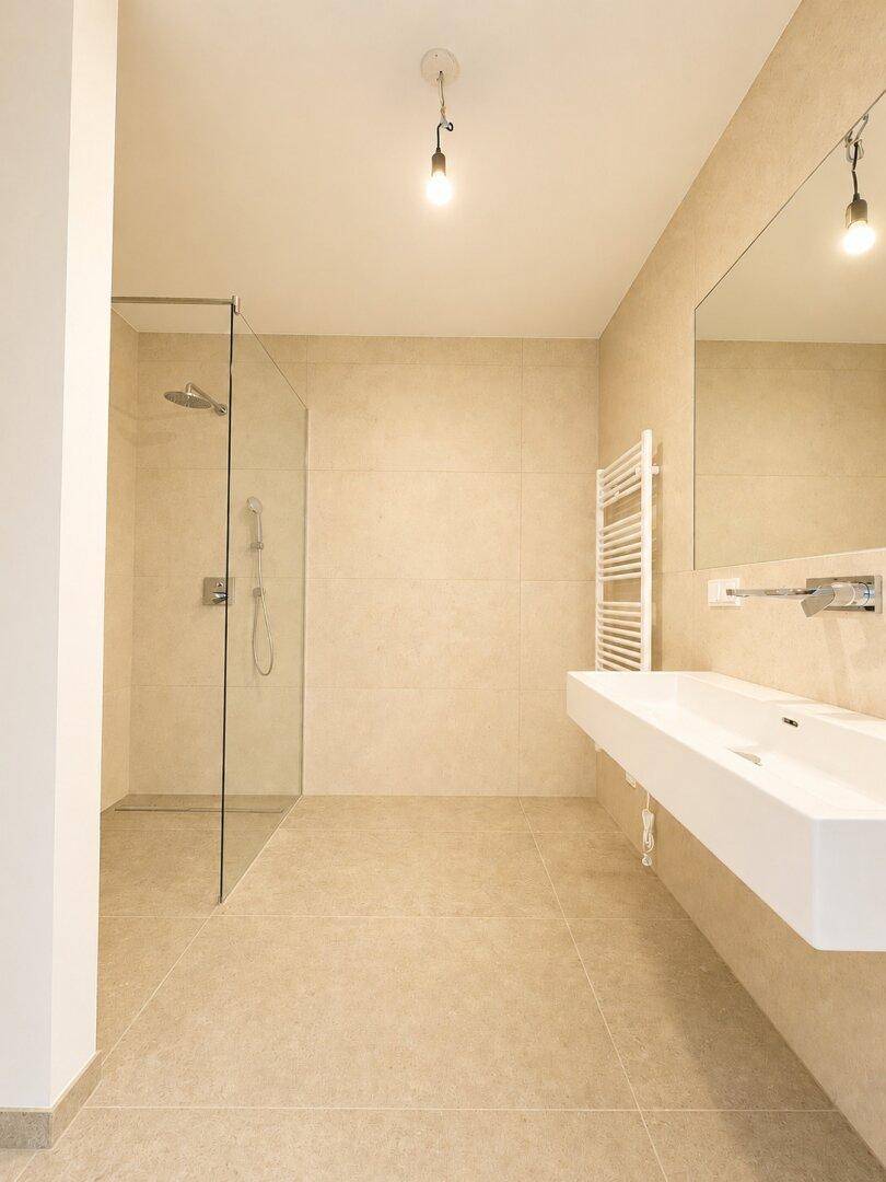 Modernes Badezimmer mit beigefarbenen Fliesen, begehbarer Dusche und Einzelwaschbecken.