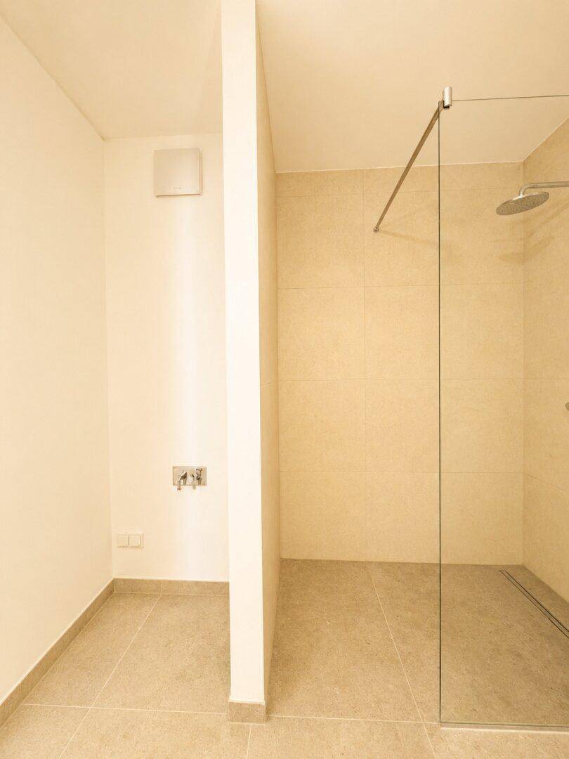 Teilansicht eines modernen Badezimmers mit begehbarer Dusche und beigefarbenen Fliesen.