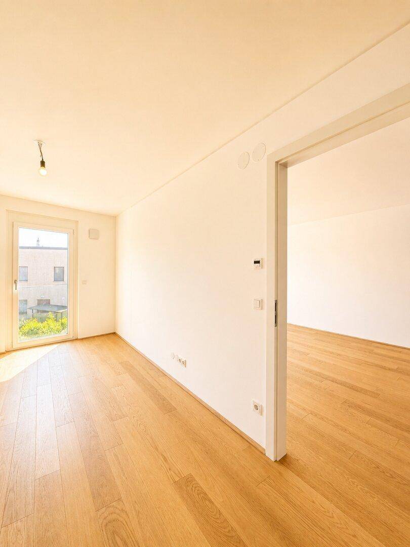 Heller Raum mit Holzboden und einem großen Fenster, das den Raum mit Licht füllt.