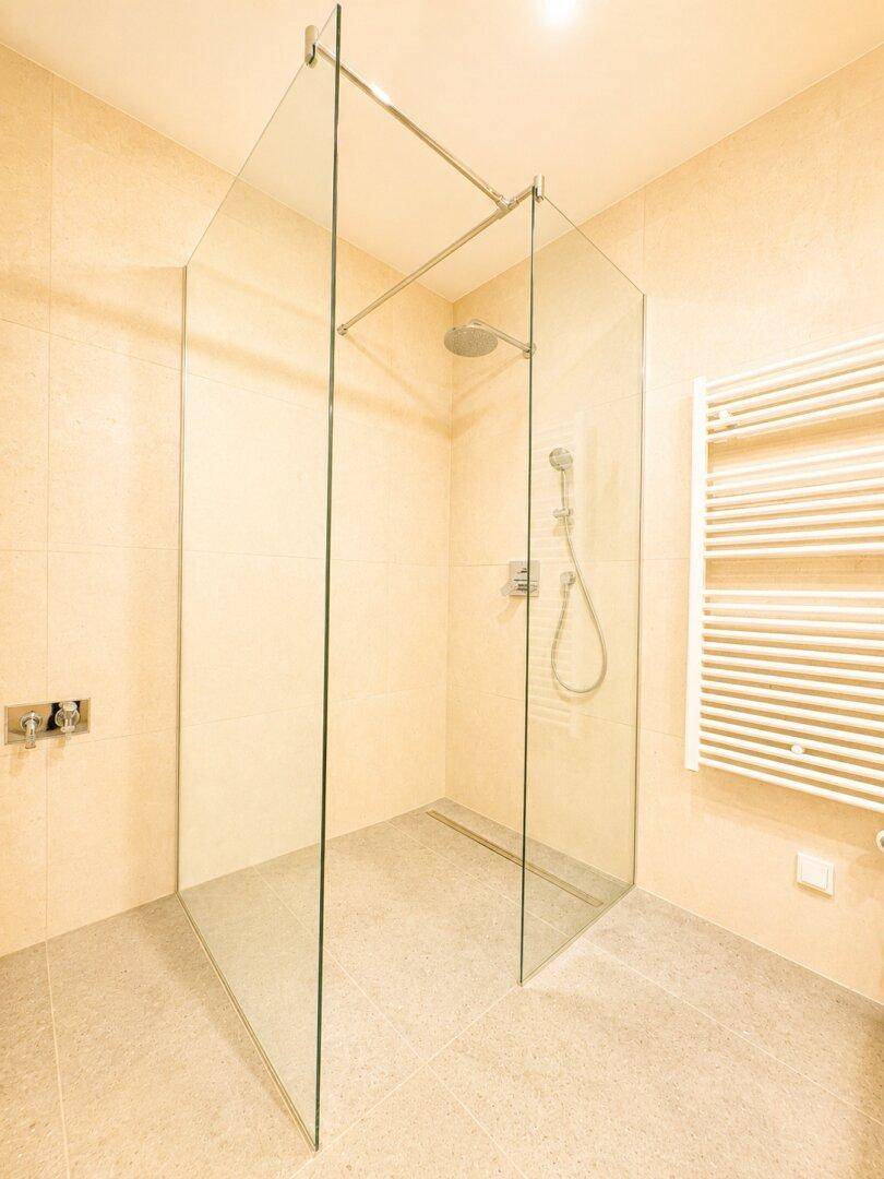 Geräumige, begehbare Dusche mit Glasabtrennung in einem modern gefliesten Badezimmer.