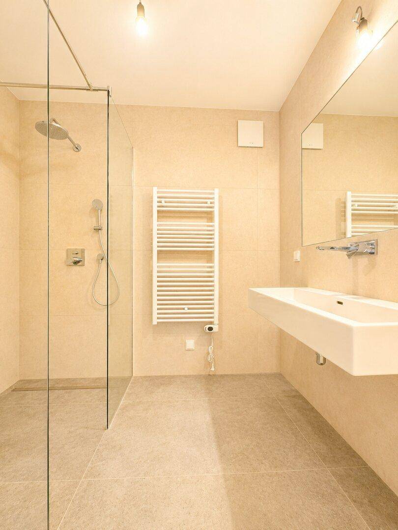 Modernes Badezimmer mit begehbarer Dusche, beigen Fliesen und beheiztem Handtuchhalter.