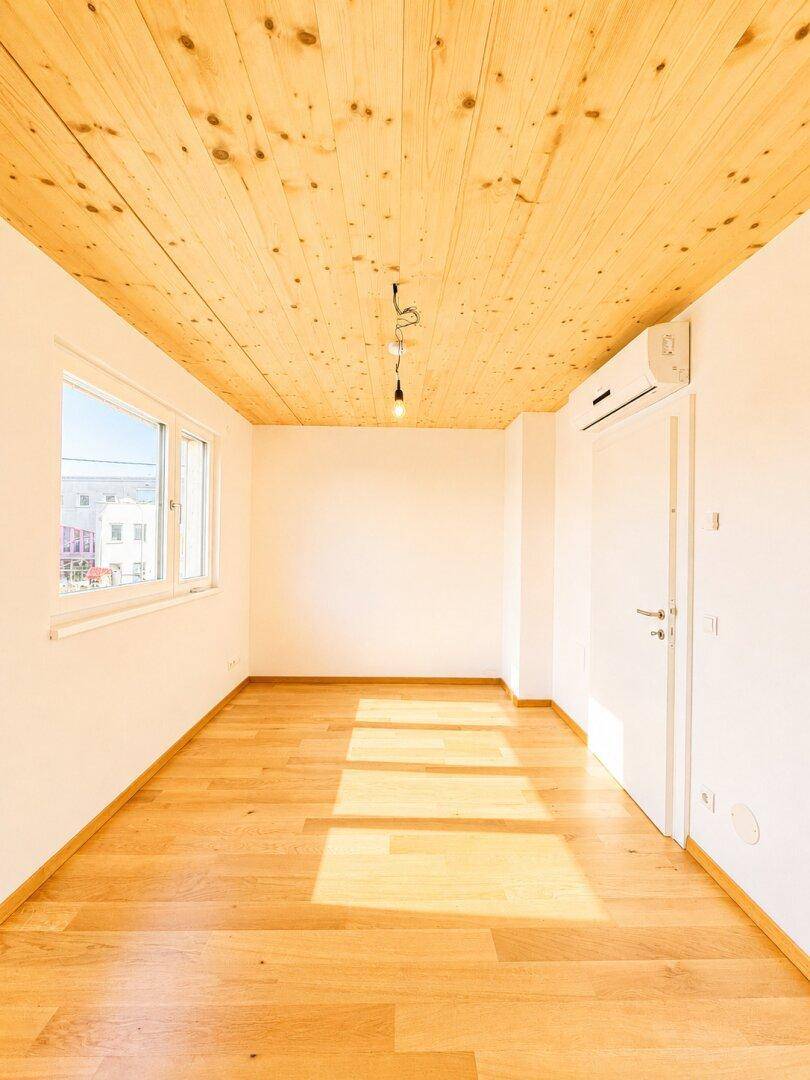 Heller Raum mit Holzboden, Holzdecke und Fenster, ausgestattet mit Klimaanlage.