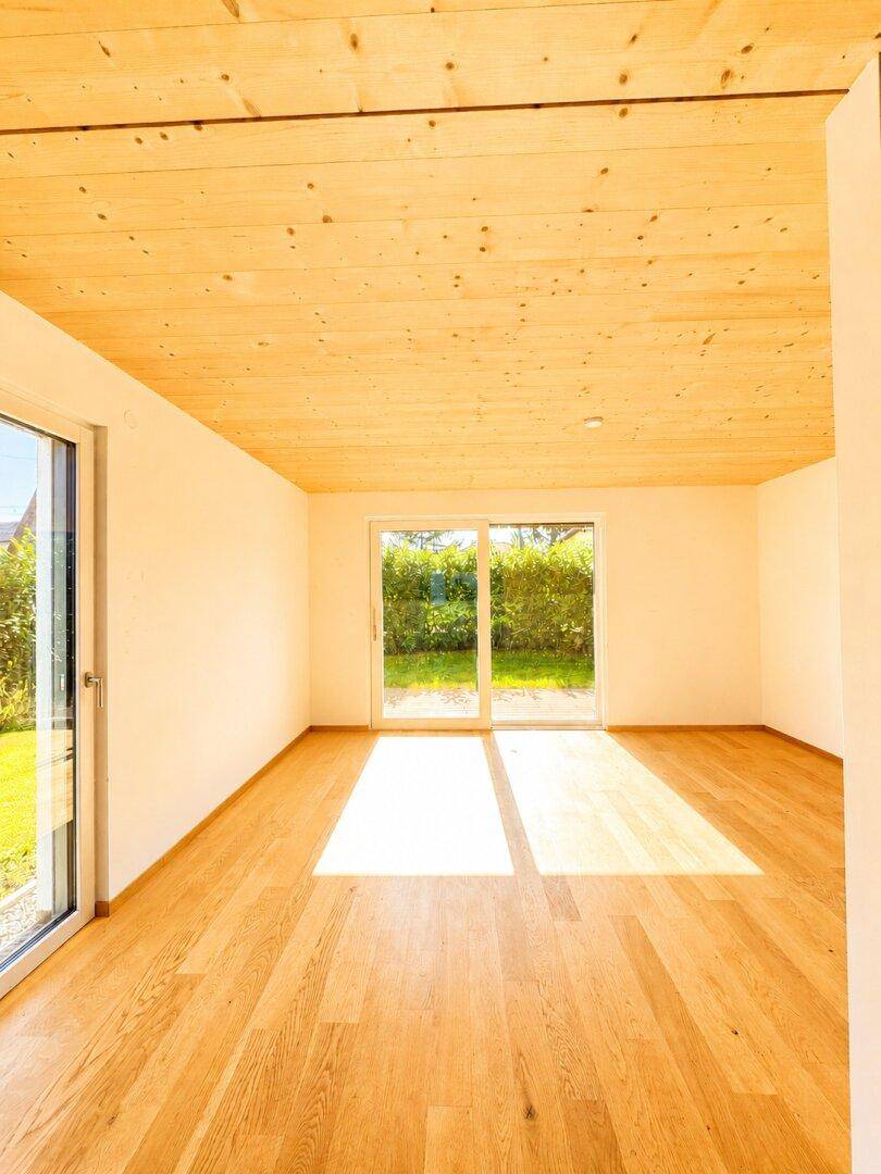 Lichtdurchfluteter Raum mit Holzboden, Holzdecke und direktem Gartenzugang.