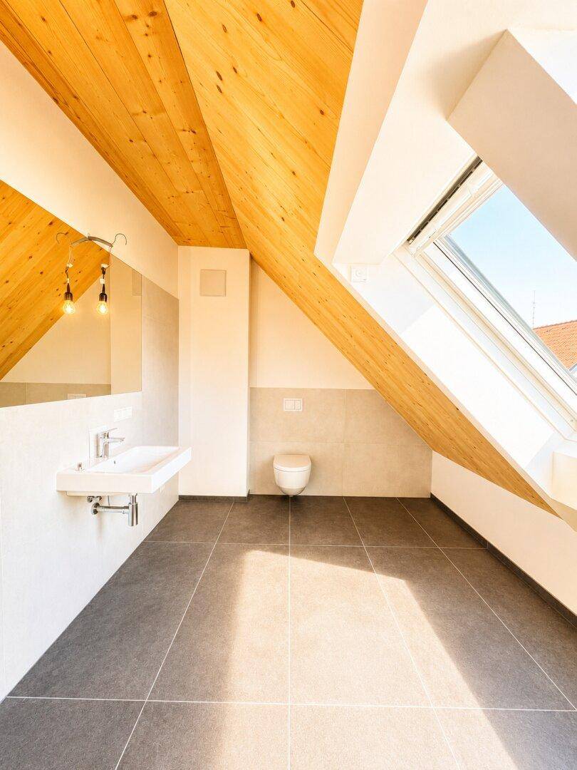 Modernes Badezimmer mit Dachschräge, Fliesenboden und Dachfenster, sehr hell.