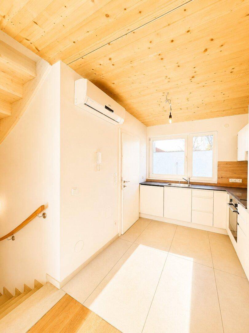 Moderne Küche mit weißen Schränken, Fliesenboden und Holztreppe, sehr hell.
