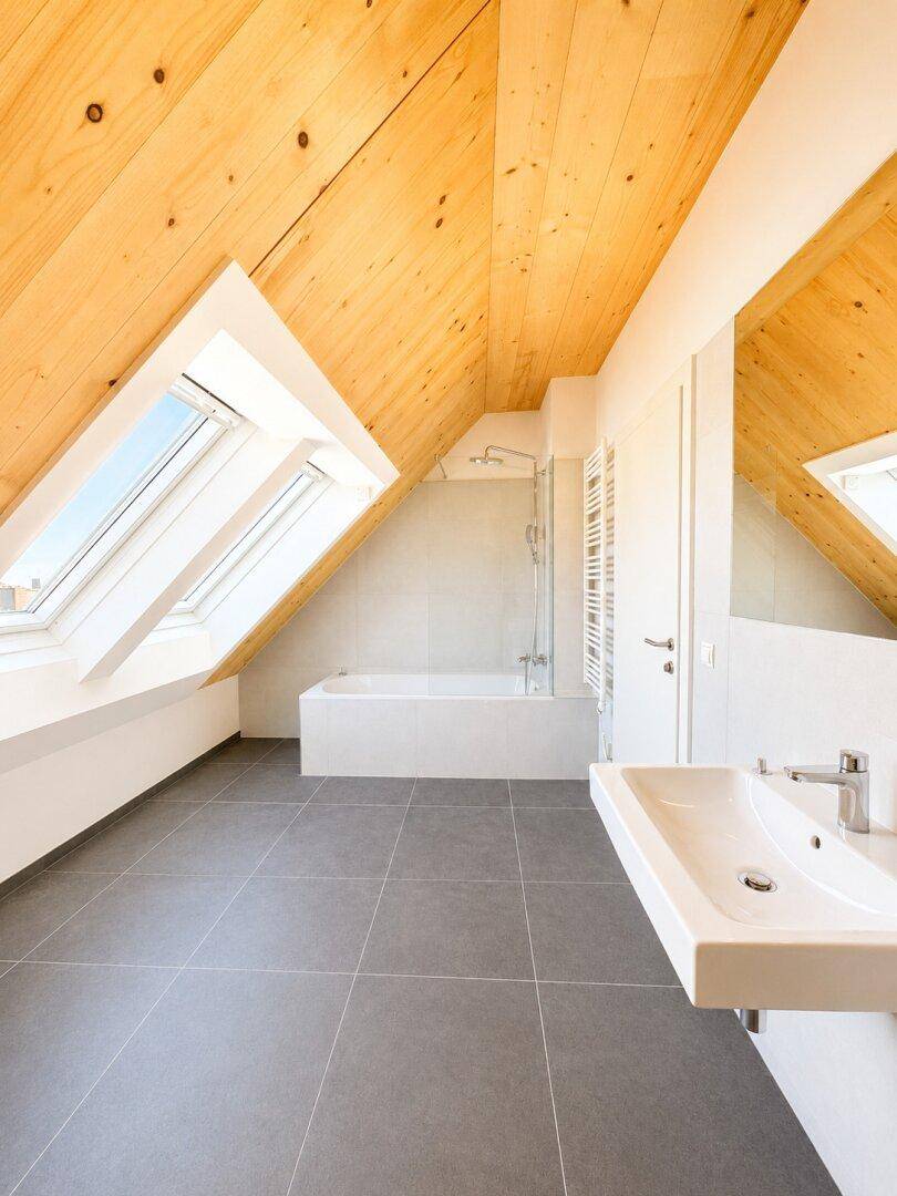 Helles Badezimmer mit Badewanne, Dachschräge und Dachfenstern, modern gefliest.