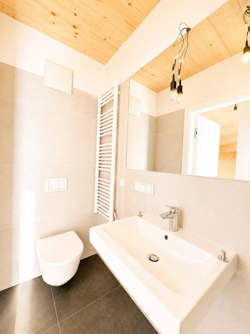 Modernes Badezimmer mit Waschbecken, Wand-WC und beheiztem Handtuchhalter, hell.