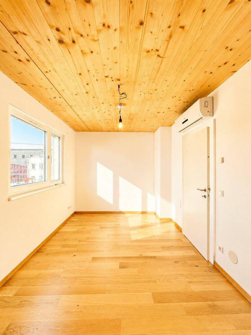 Heller Raum mit Holzboden, Holzdecke und Fenster, ausgestattet mit Klimaanlage.