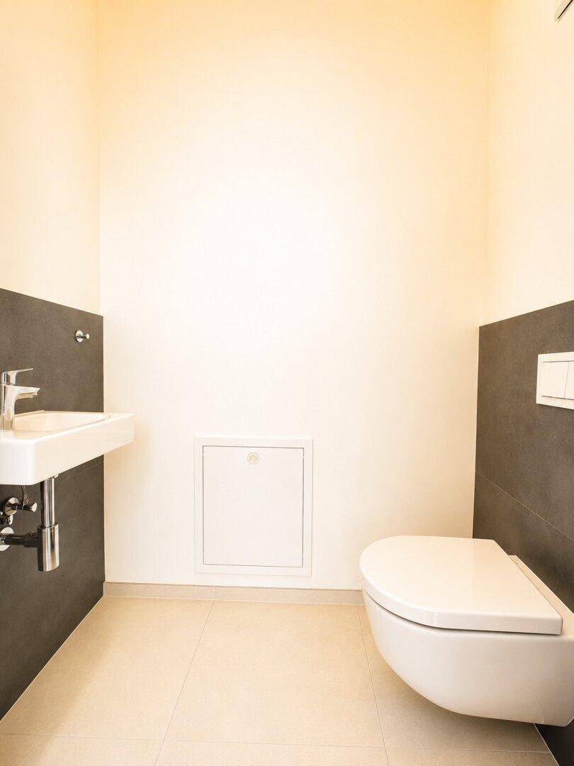 Modernes Gäste-WC mit Wand-WC und kleinem Waschbecken, in hellen Farben.