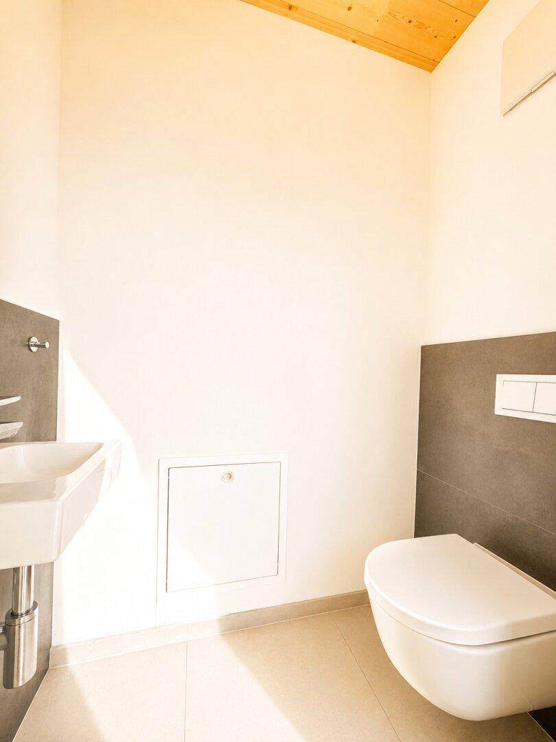 Helles Gäste-WC mit modernem Wand-WC und kleinem Waschbecken, sauber und funktional.