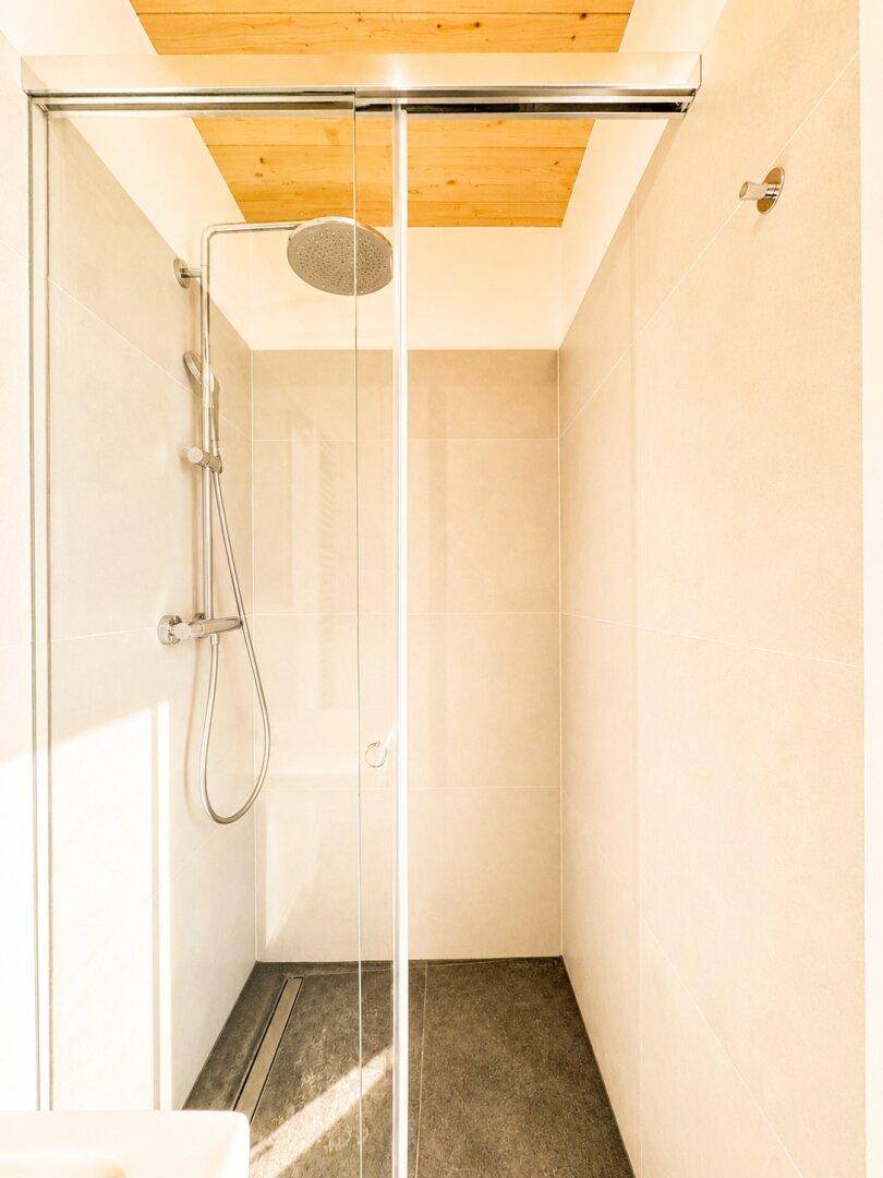 Moderne begehbare Dusche mit Glasabtrennung und Regenduschkopf, hell gefliest.