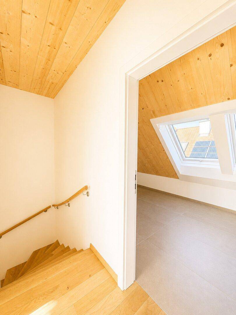 Heller Treppenbereich mit Holzboden, der zu einem Raum mit Dachfenstern führt.