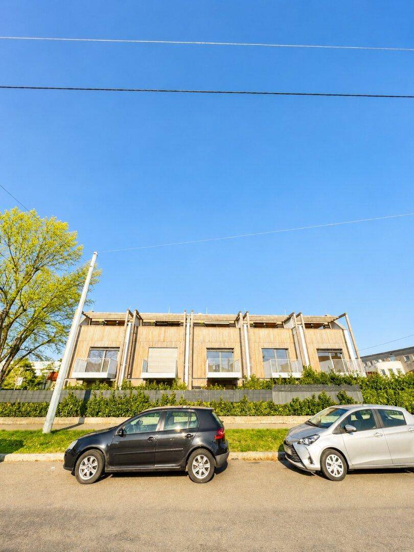 Moderne Reihenhäuser mit Holzfassade und Balkonen unter blauem Himmel.
