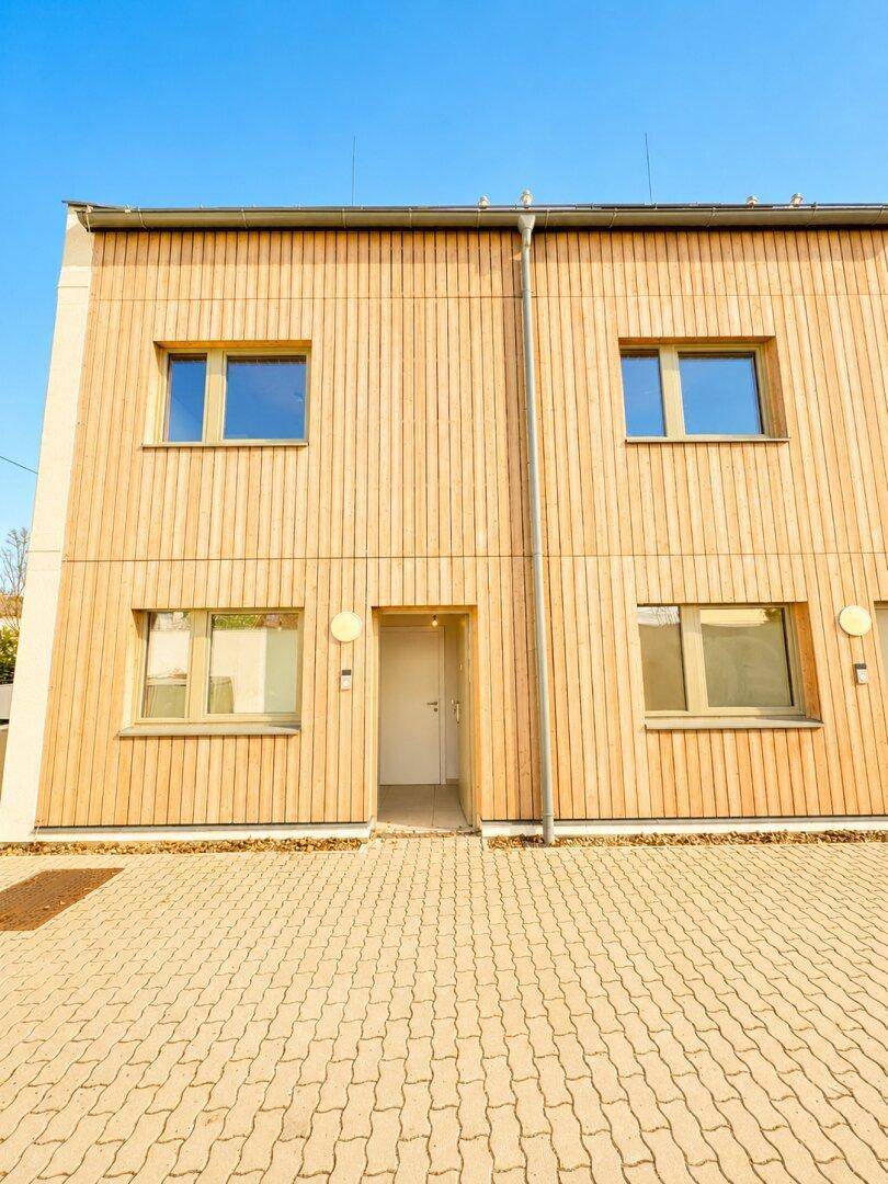 Moderne Hausfassade mit Holzverkleidung und gepflastertem Eingangsbereich.