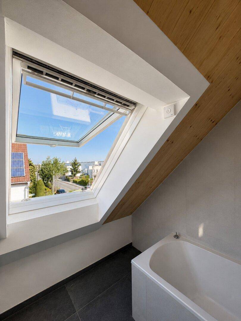 Modernes Badezimmer im Dachgeschoss mit Badewanne, Dachfenster und Blick ins Grüne.