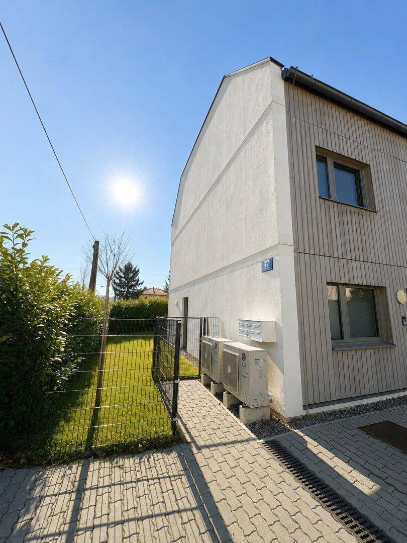 Eckansicht eines modernen Gebäudes mit weißer Fassade und Holzdetails, angrenzend an eine Rasenfläche.
