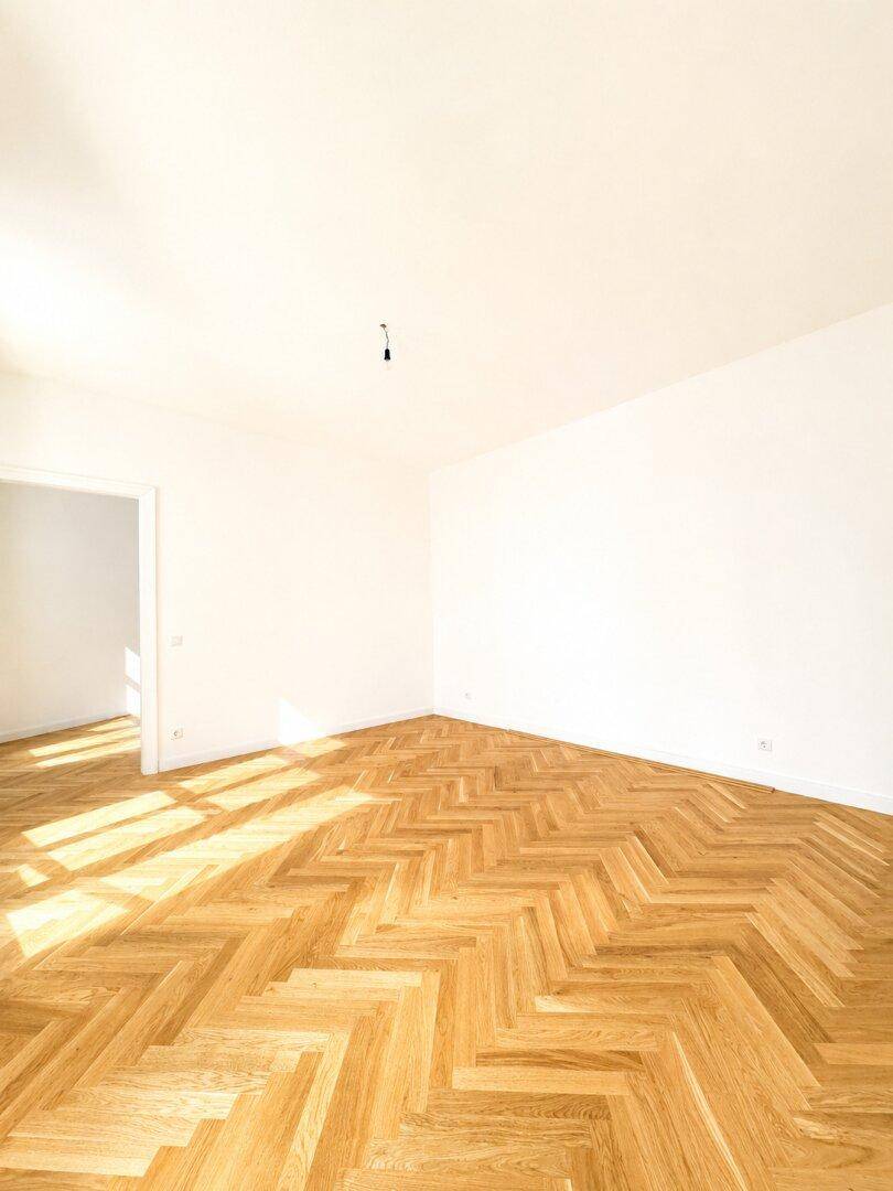 Geräumiges, helles Zimmer mit elegantem Fischgrätparkett und weißen Wänden, ideal für individuelle Gestaltung.