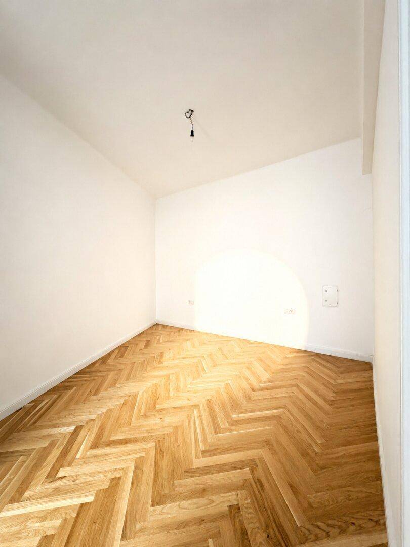 Kleineres, helles Zimmer mit Fischgrätparkett und weißen Wänden, ideal als Schlaf- oder Arbeitszimmer.