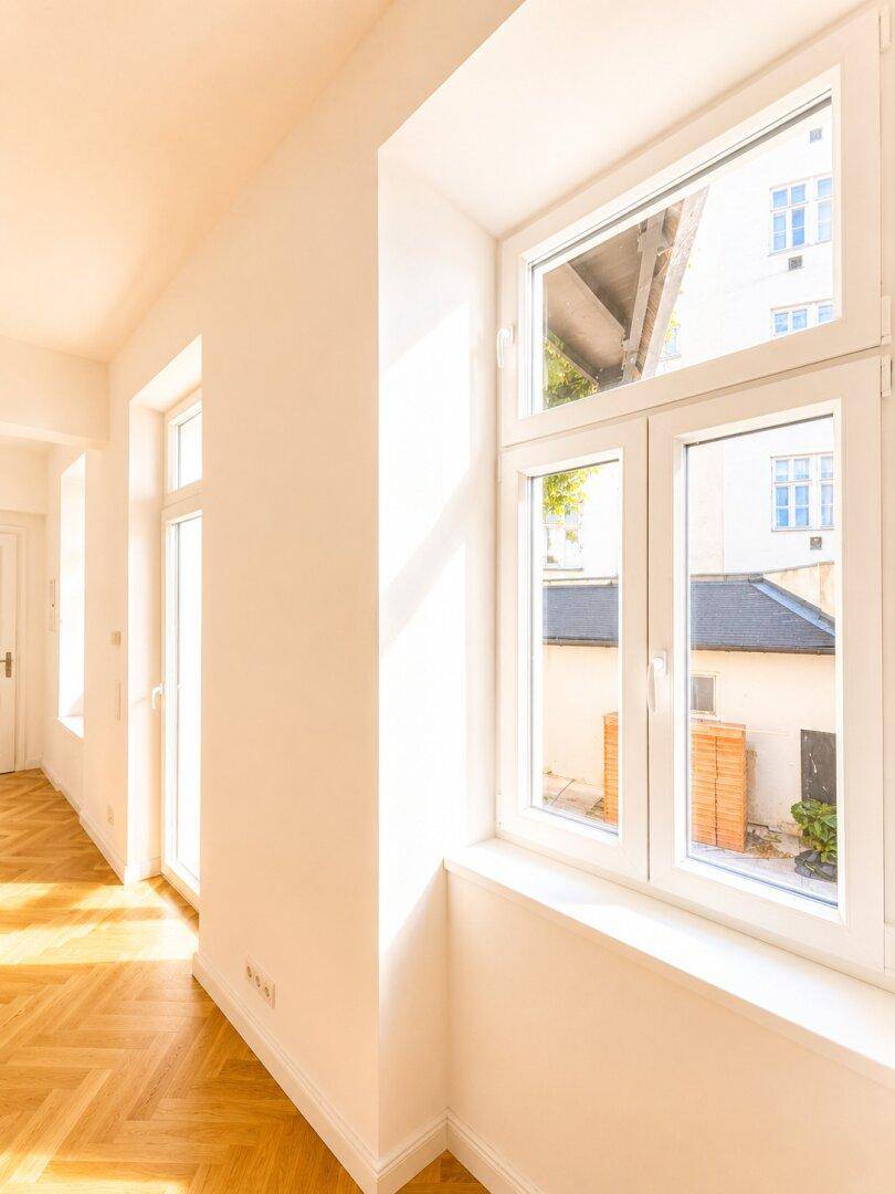 Heller Bereich mit Fischgrätparkett und großem Fenster, das einen Blick auf den Innenhof freigibt.
