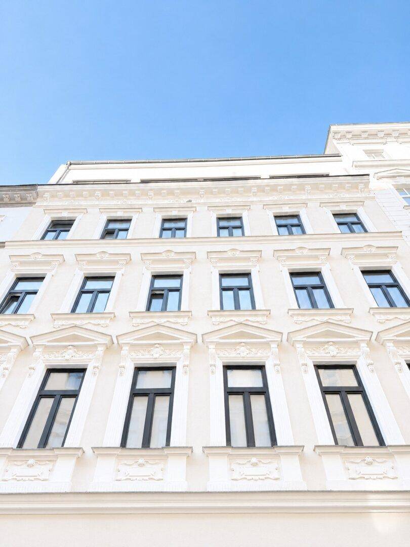 Klassische weiße Gebäudefassade mit vielen Fenstern und eleganten architektonischen Details unter blauem Himmel.