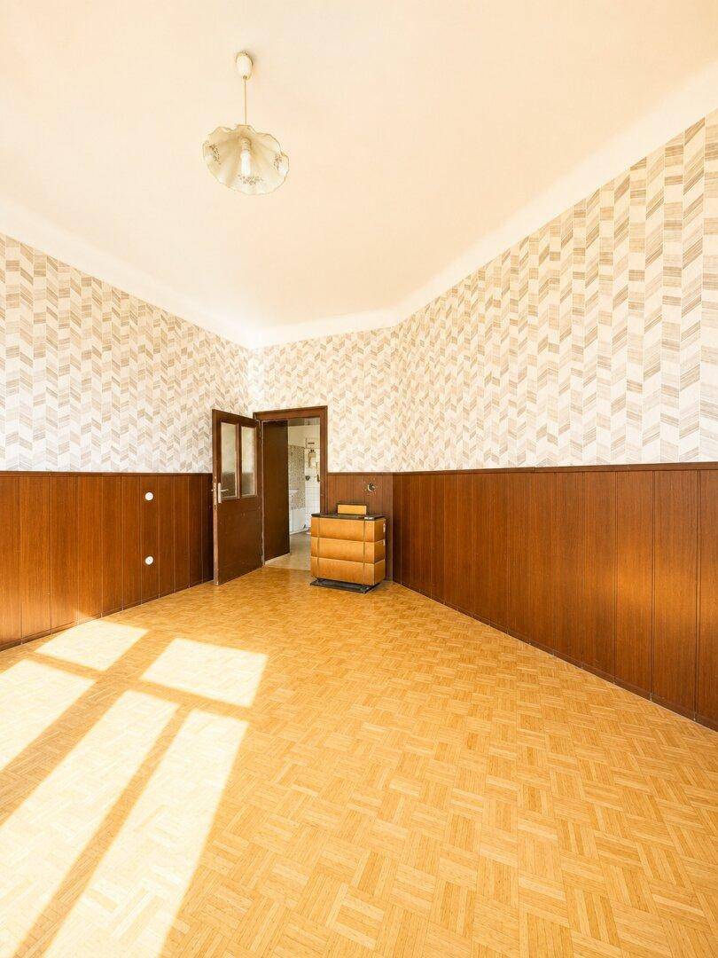 Heller Raum mit Parkettboden, Holzvertäfelung und einer offenen Tür zu einem weiteren Zimmer.