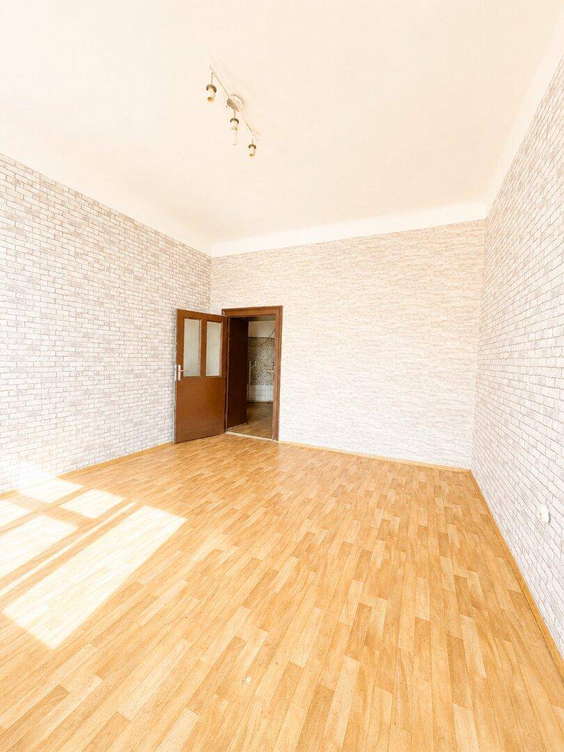 Leeres Zimmer mit Parkettboden, Ziegelstein-Tapete und einer braunen Tür.