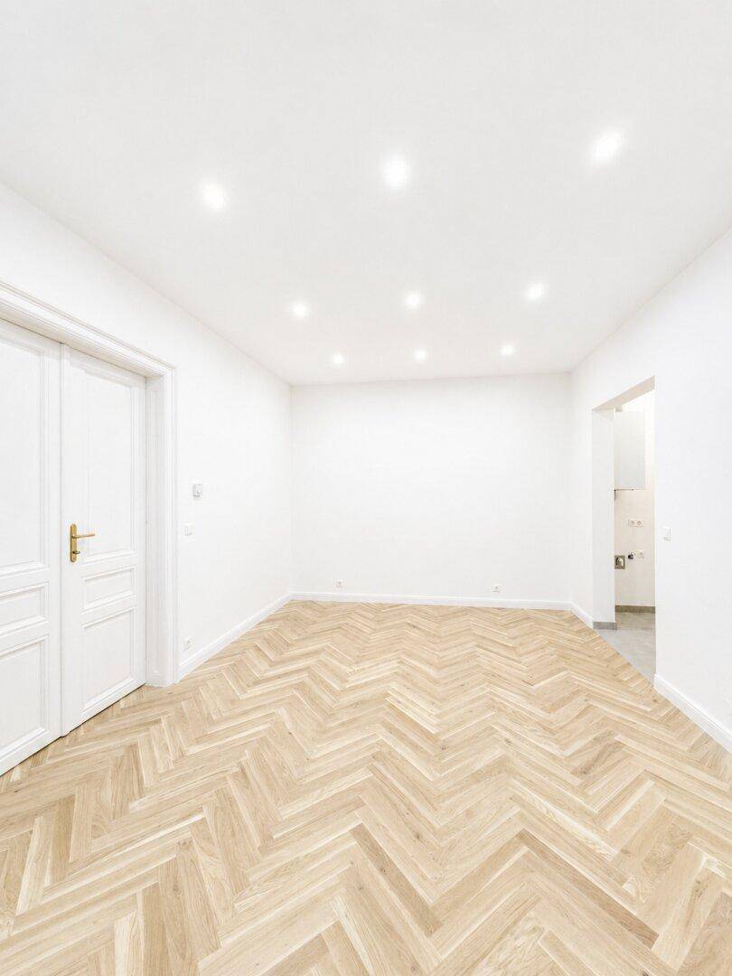 Leeres Zimmer mit neuem Fischgrätparkett und weiß gestrichenen Wänden, bereit zum Einzug.