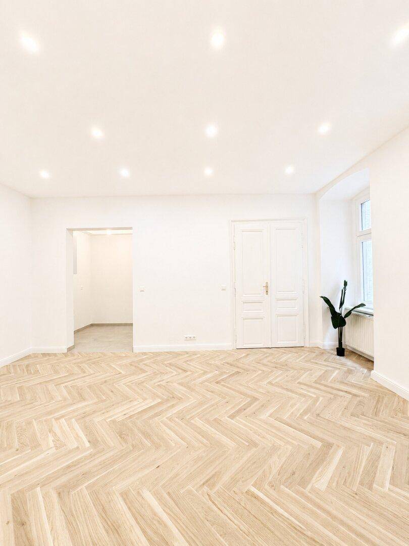 Großzügiges Zimmer mit Fischgrätparkett und Zugang zu weiteren Räumen, hell und einladend.