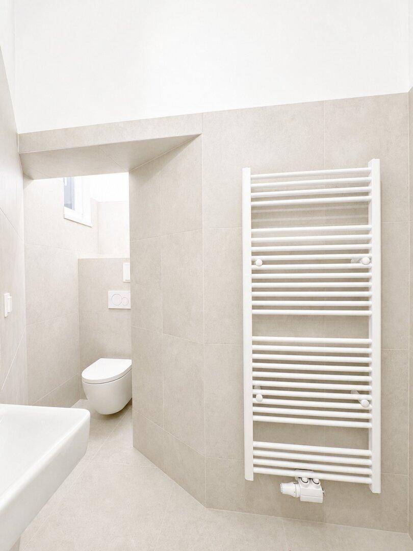 Modernes Badezimmer mit beigefarbenen Fliesen, wandhängendem WC und Handtuchheizkörper.