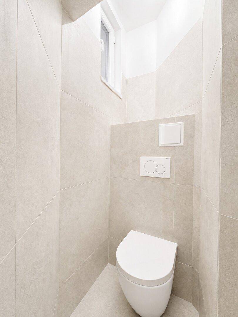 Helles, separates WC mit modernem wandhängendem WC und kleinem Fenster.