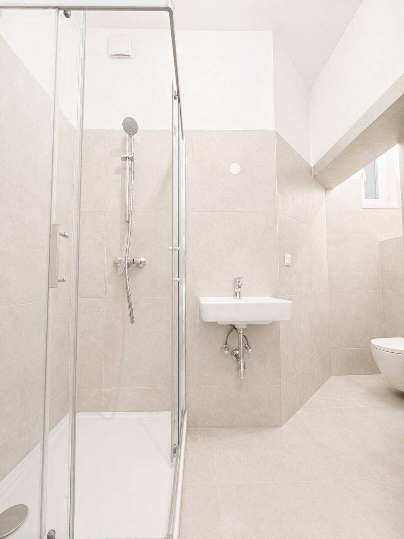 Modernes Badezimmer mit Duschkabine, Waschbecken und beigefarbenen Fliesen.