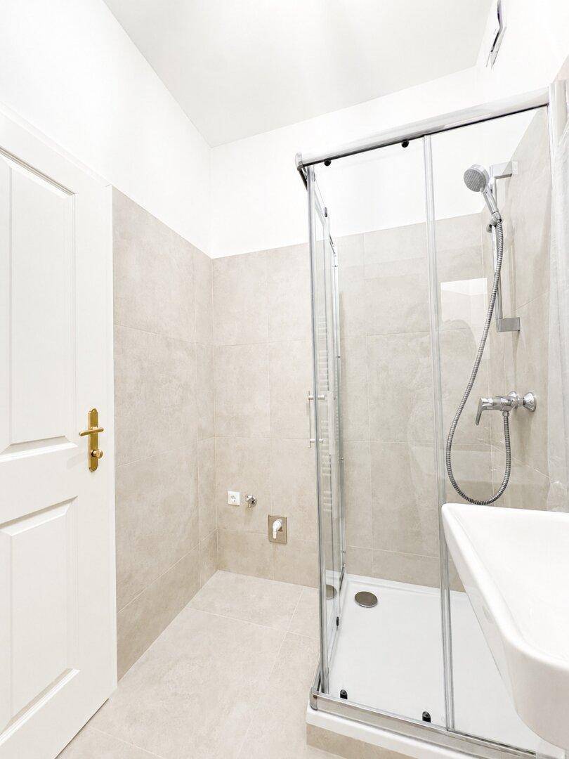 Helles Badezimmer mit Duschkabine, Waschbecken und beigefarbenen Wand- und Bodenfliesen.