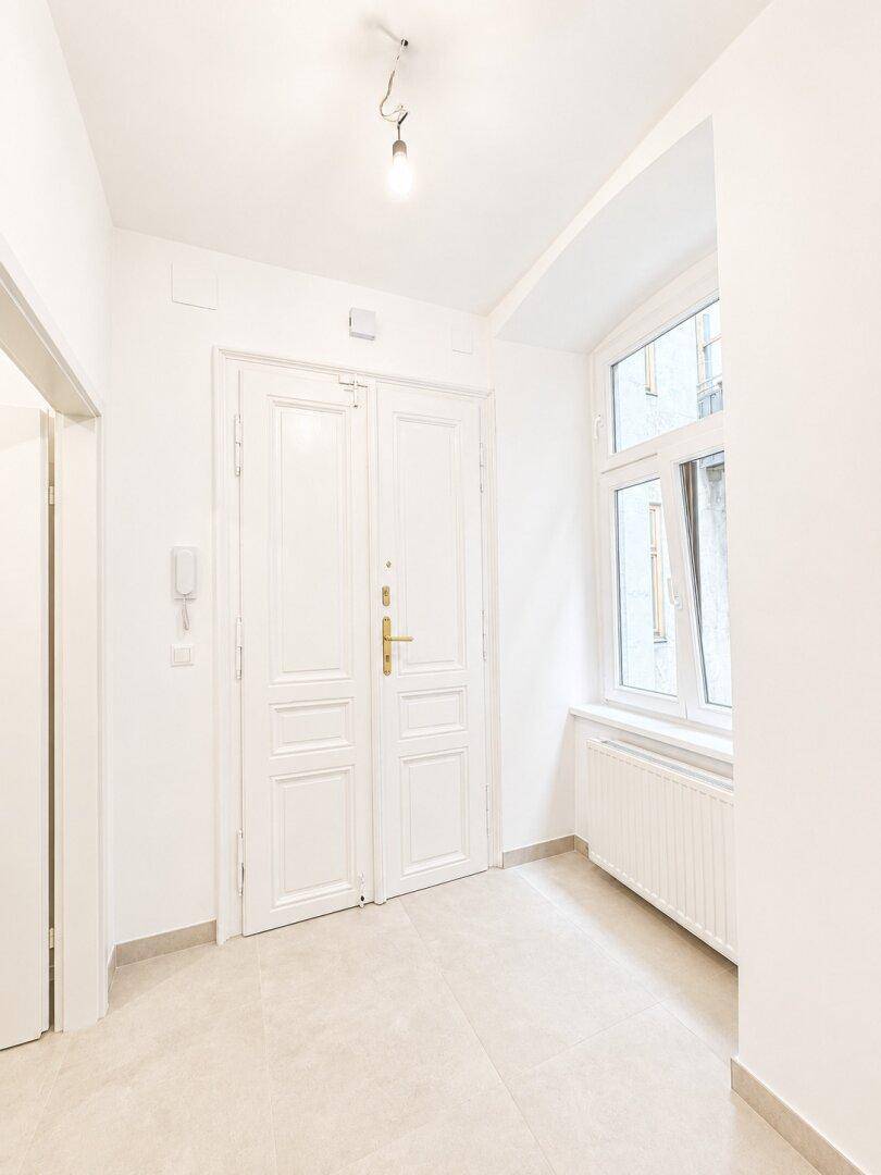 Freundlicher Eingangsbereich mit Fliesenboden, weißer Doppeltür und großem Fenster.