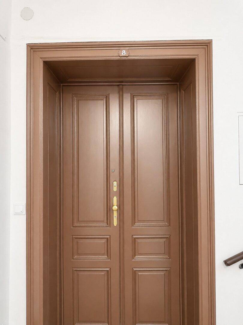 Klassische braune Eingangstür mit goldener Klinke in einem Mehrfamilienhaus.