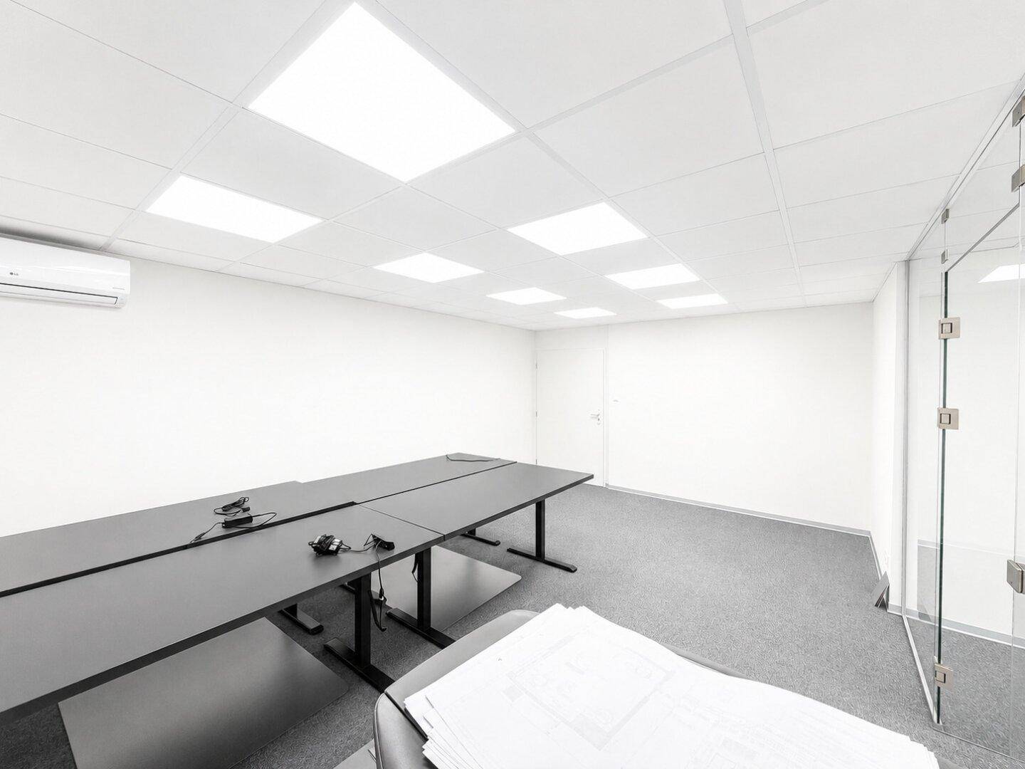 Moderner Konferenzraum mit großem Tisch, grauem Teppichboden und Klimaanlage.