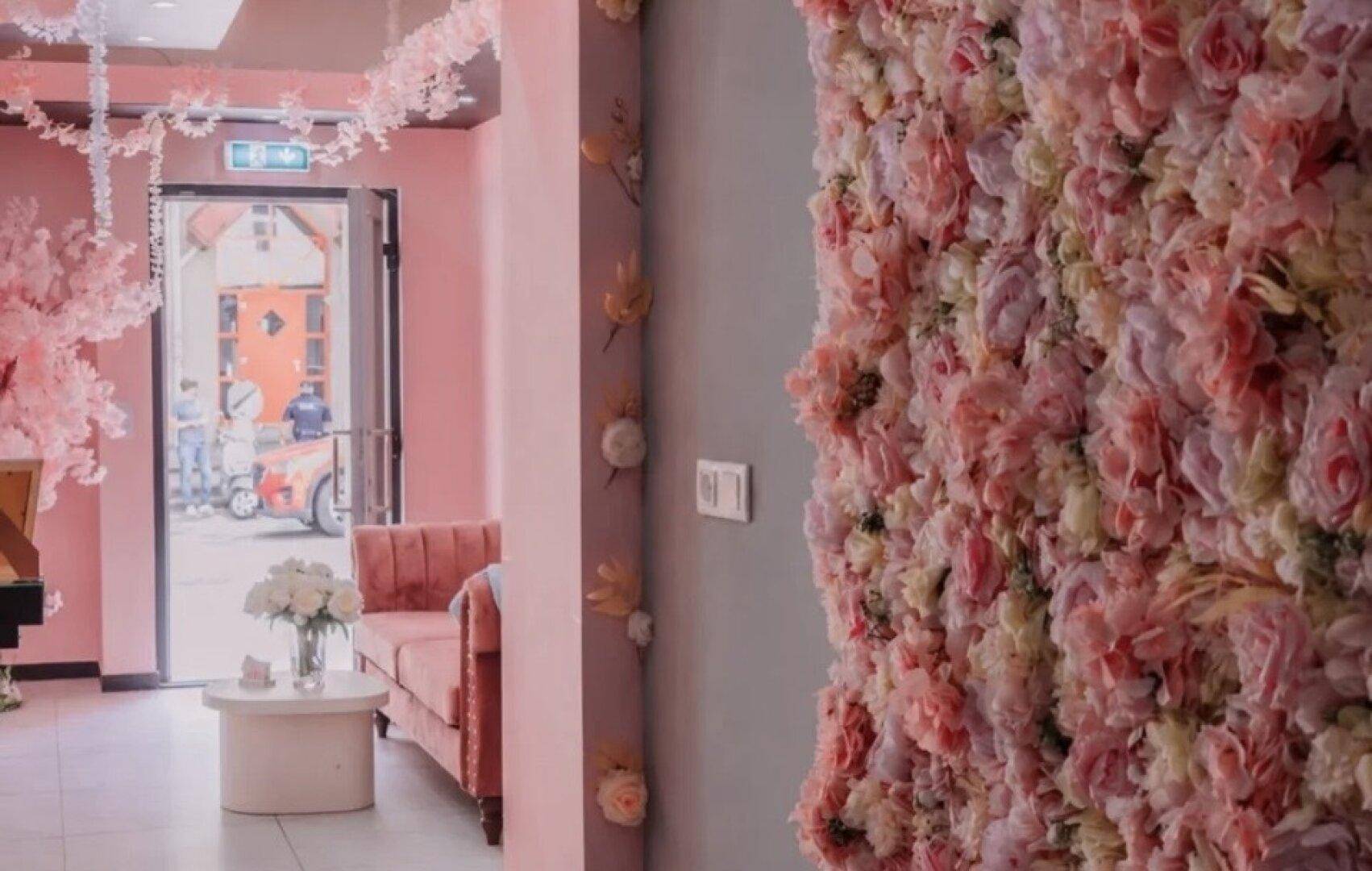 Empfangsbereich mit floraler Wanddekoration, rosa Samtsofa und Blick auf die Straße durch die Tür.