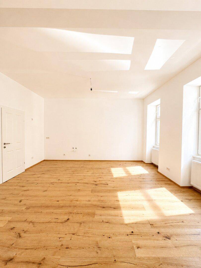 Geräumiges, helles Zimmer mit Holzboden und mehreren Fenstern, das viel natürliches Licht erhält.
