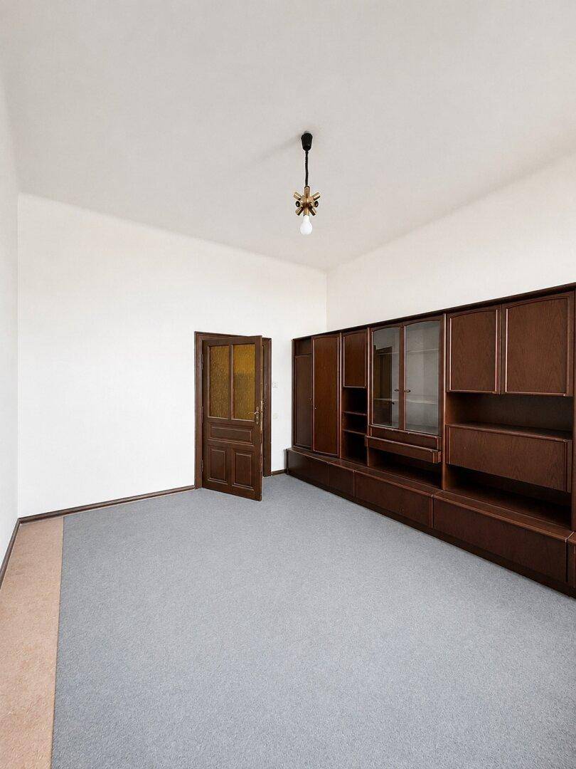 Leeres Wohnzimmer mit Holzboden, einer großen dunklen Schrankwand und einer passenden Holztür.