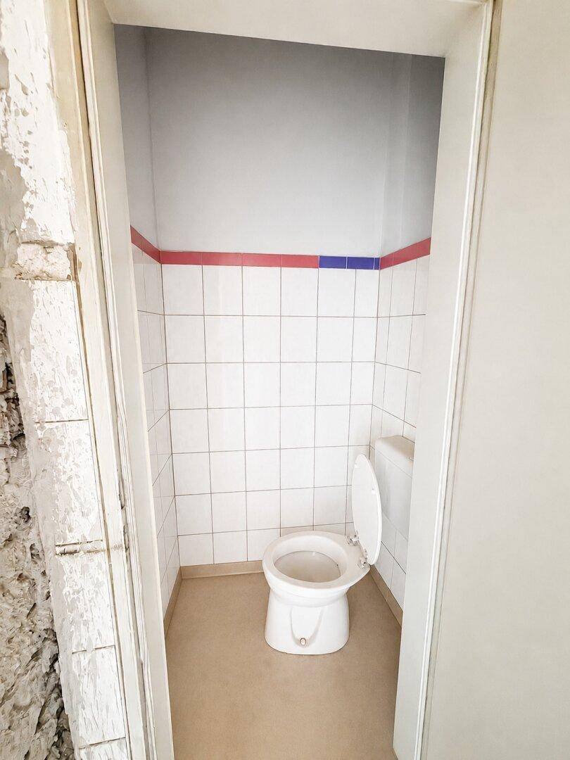 Kleines WC mit weißen Fliesen, roten und blauen Akzenten sowie einer einfachen Toilette.