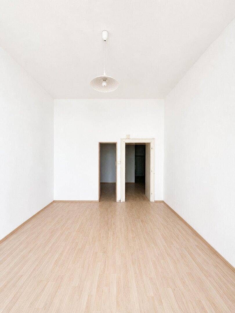 Heller, leerer Raum mit hellem Holzboden und weißen Wänden, bietet Zugang zu zwei weiteren Zimmern.