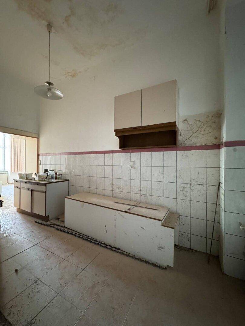 Renovierungsbedürftige Küche mit alten Fliesen, beschädigten Schränken und sichtbaren Wasserschäden an der Decke.