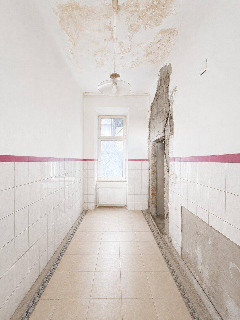 Langer, gefliester Flur mit dekorativem Bodenrand und Fenster, zeigt Wasserschäden an der Decke.