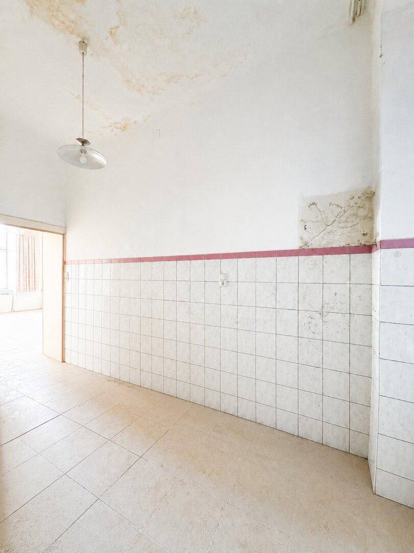 Leerer, gefliester Raum mit Wasserschäden an der Decke, der auf eine bevorstehende Renovierung wartet.