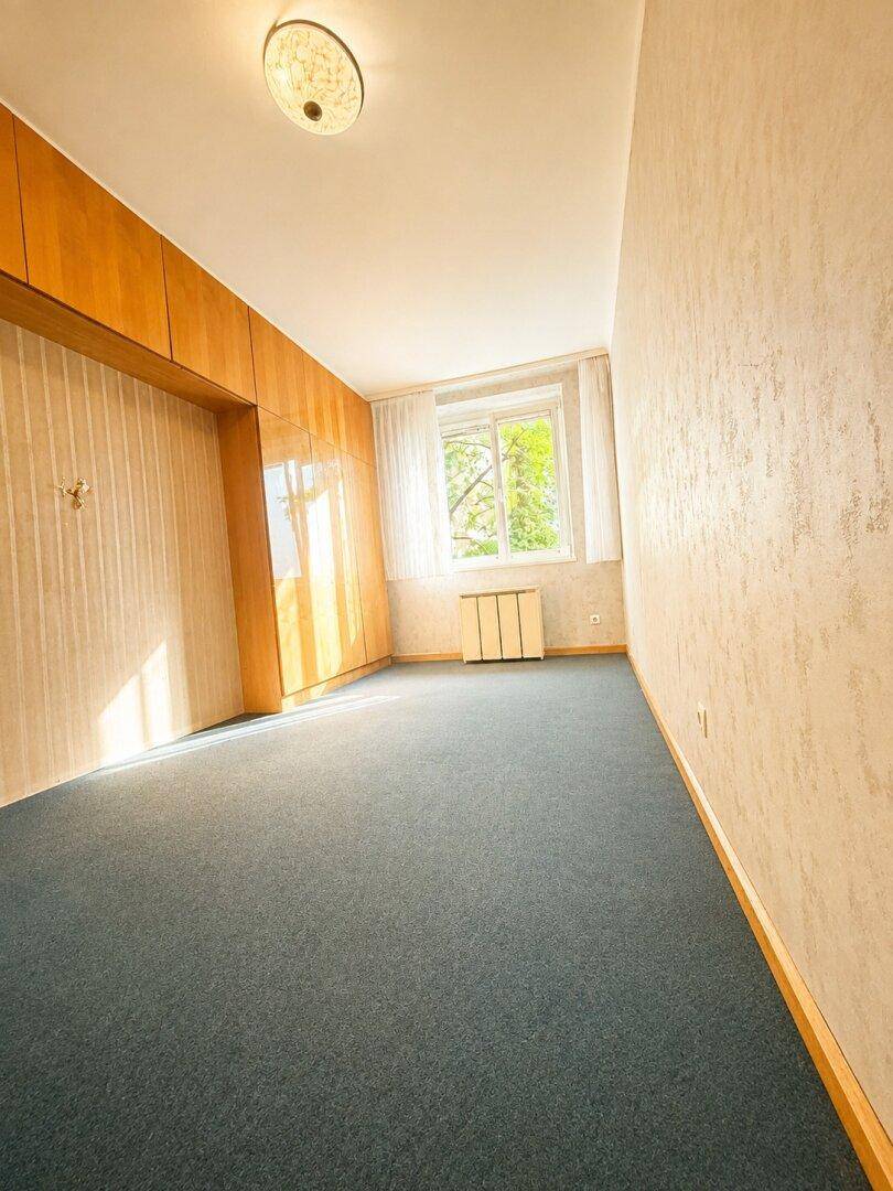 Geräumiges Schlafzimmer mit blauem Teppichboden, Holzschränken und einem Fenster mit Blick ins Grüne.