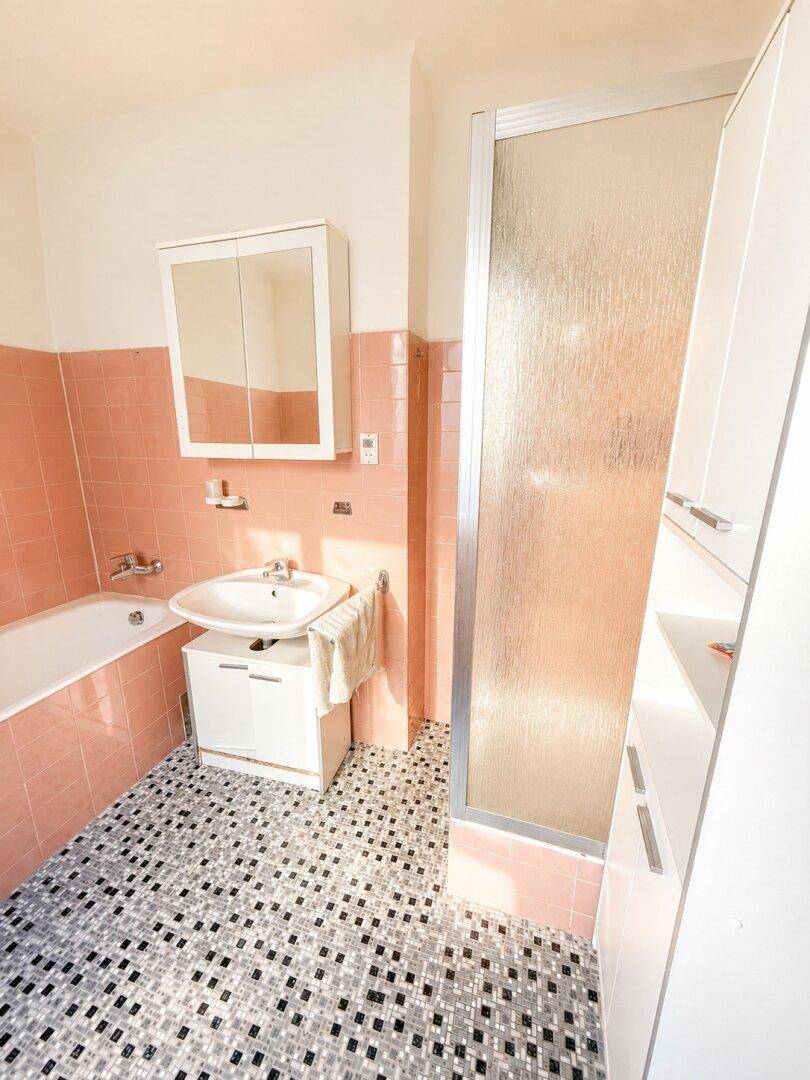 Retro-Badezimmer mit rosa Wandfliesen, Badewanne und Duschkabine, gut erhalten.
