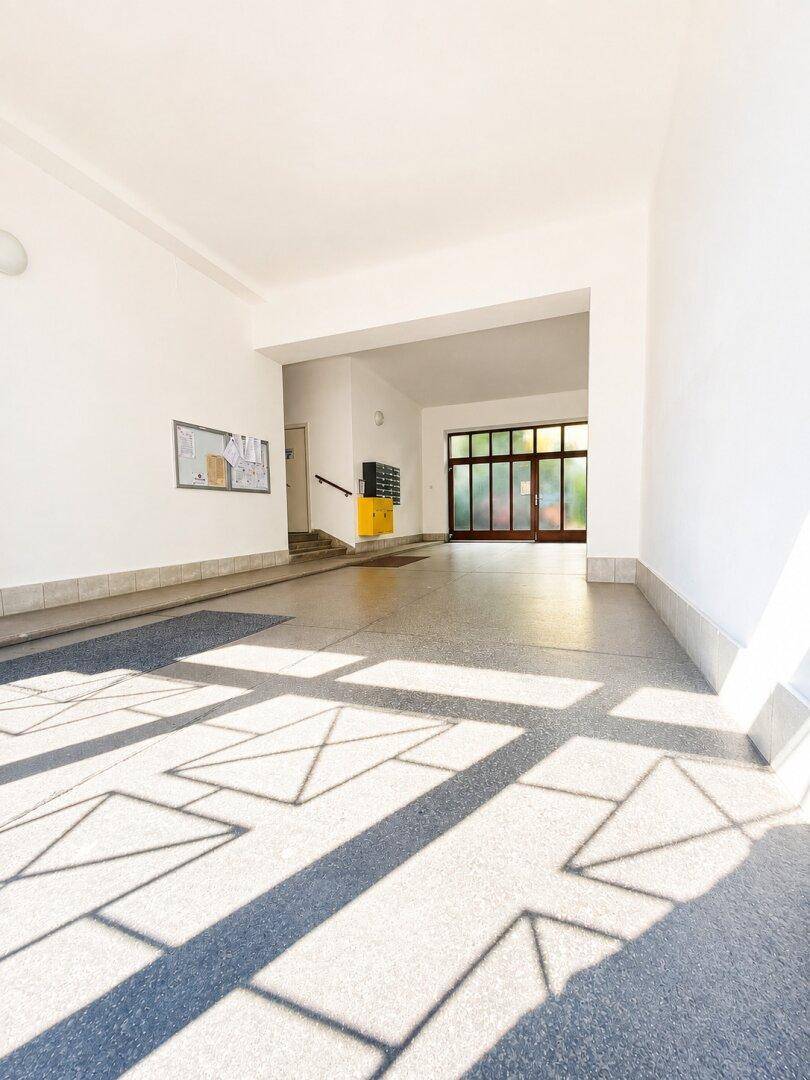 Heller Eingangsbereich eines Mehrfamilienhauses mit Terrazzoboden und großen Glastüren.